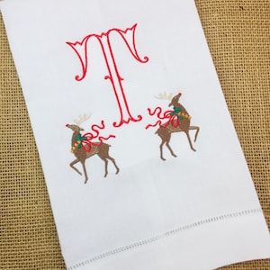 May include: White hand towel with red embroidered letter T and two brown reindeer with red bows and green holly.
