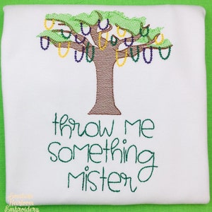 May include: A white t-shirt with green embroidery of a tree with purple and yellow beads hanging from the branches. The text "Throw me something mister" is embroidered below the tree.
