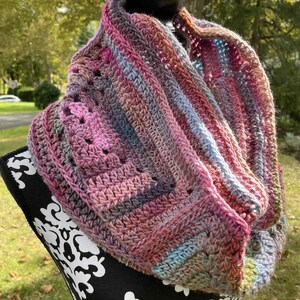 May include: A crocheted infinity scarf in shades of pink, purple, and blue. The scarf is made with a textured stitch and has a slightly frayed edge.