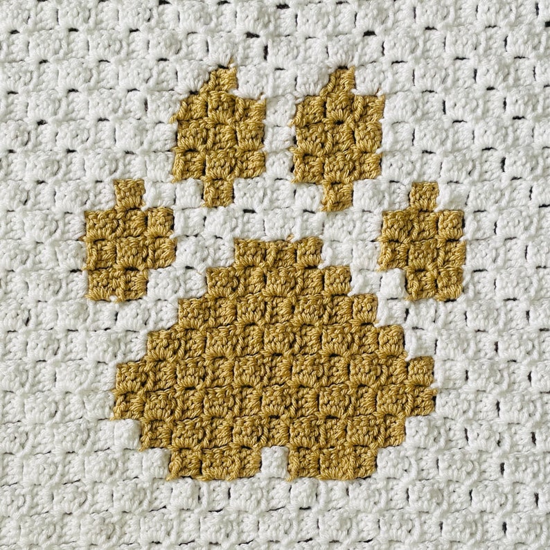 May include: A white crocheted blanket with a large golden brown paw print in the center.