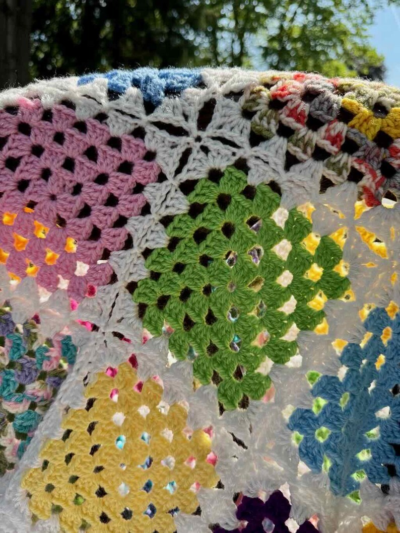 May include: Close-up of a colorful, handmade crochet blanket. The blanket features a patchwork design with various colors, including pink, green, yellow, blue, and white. The crochet stitches create a textured, geometric pattern.