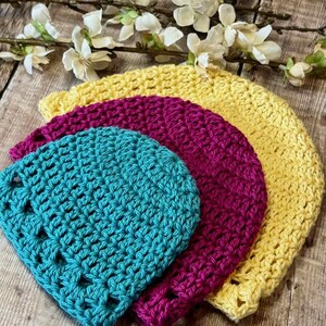 May include: Three stacked crochet hats in bright colors. The smallest hat is teal, the middle hat is magenta, and the largest hat is yellow. Each hat features a consistent, textured stitch pattern throughout, creating a layered, circular appearance.