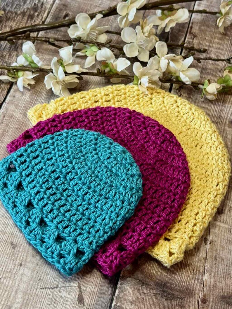 May include: Three stacked crochet hats in bright colors. The smallest hat is teal, the middle hat is magenta, and the largest hat is yellow. Each hat features a consistent, textured stitch pattern throughout, creating a layered, circular appearance.