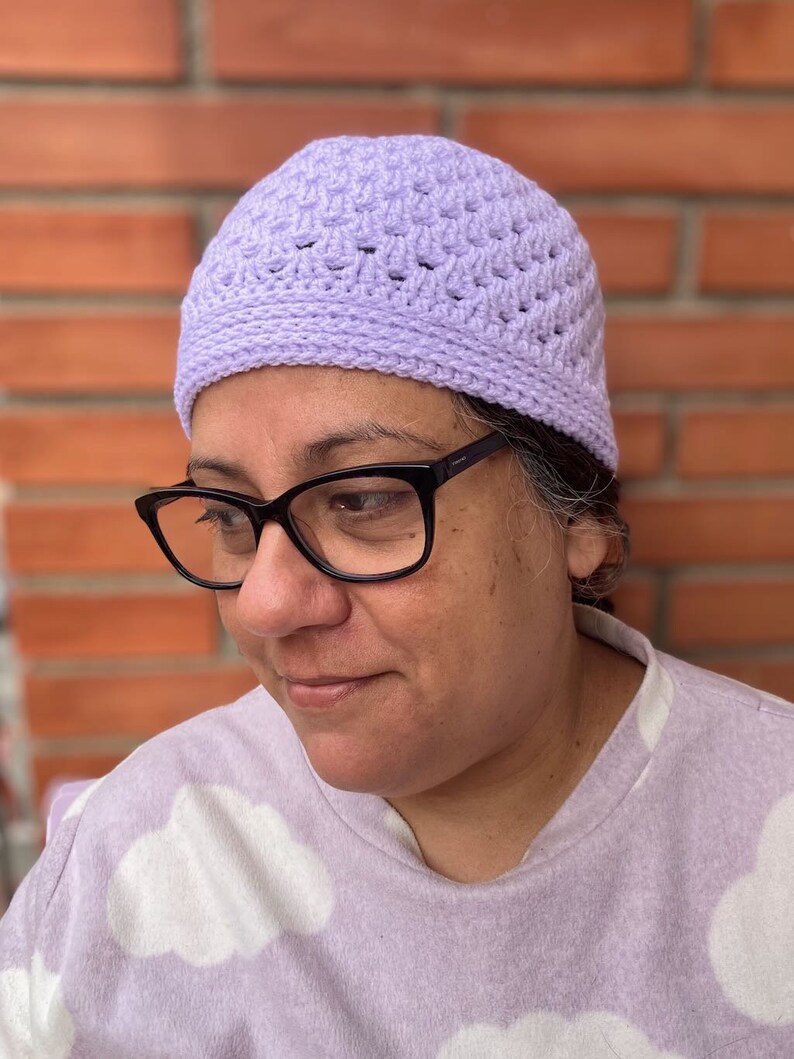 Pu&ograve; includere: Primo piano di una persona che indossa un berretto di lana color lilla chiaro. Il berretto ha un semplice motivo a maglia e viene indossato sulla testa della persona.