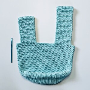 May include: A light blue crocheted tote bag with two straps. The bag is made with a single crochet stitch and has a square shape.