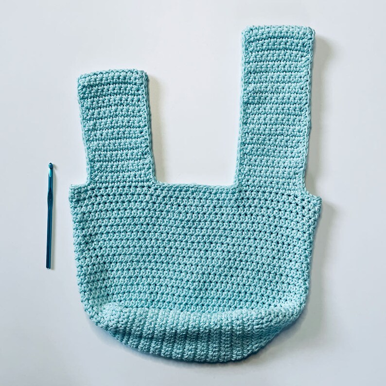 May include: A light blue crocheted tote bag with two straps. The bag is made with a single crochet stitch and has a square shape.