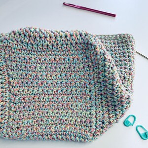 May include: A crocheted square made with a multi-colored yarn in shades of pink, blue, and yellow.