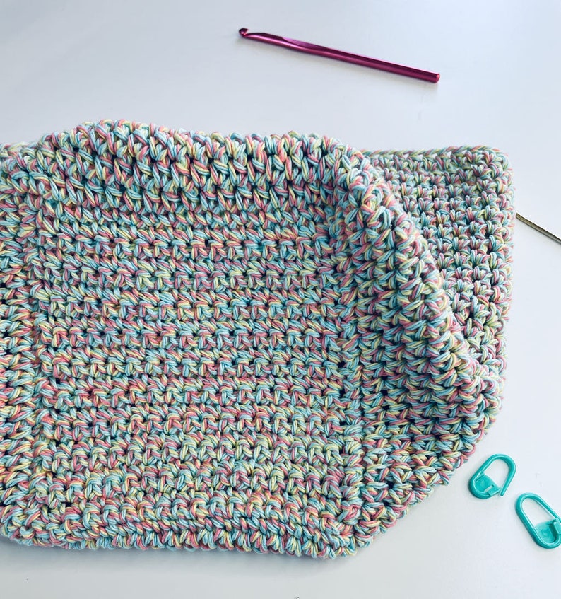 May include: A crocheted square made with a multi-colored yarn in shades of pink, blue, and yellow.