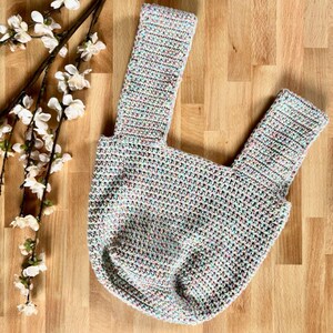 May include: A crocheted tote bag with a light blue, pink, and green color scheme. The bag has two straps and a wide, open top.