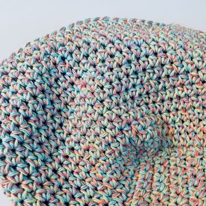 May include: Close-up of a crocheted fabric with a multi-colored yarn in shades of pink, blue, and yellow.