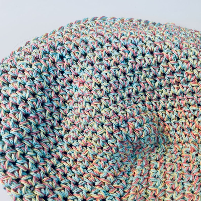 May include: Close-up of a crocheted fabric with a multi-colored yarn in shades of pink, blue, and yellow.