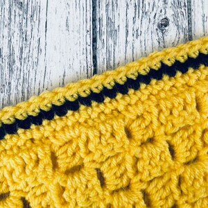 May include: Close-up of a yellow crocheted fabric with a black crocheted border. The fabric has a textured, woven pattern.