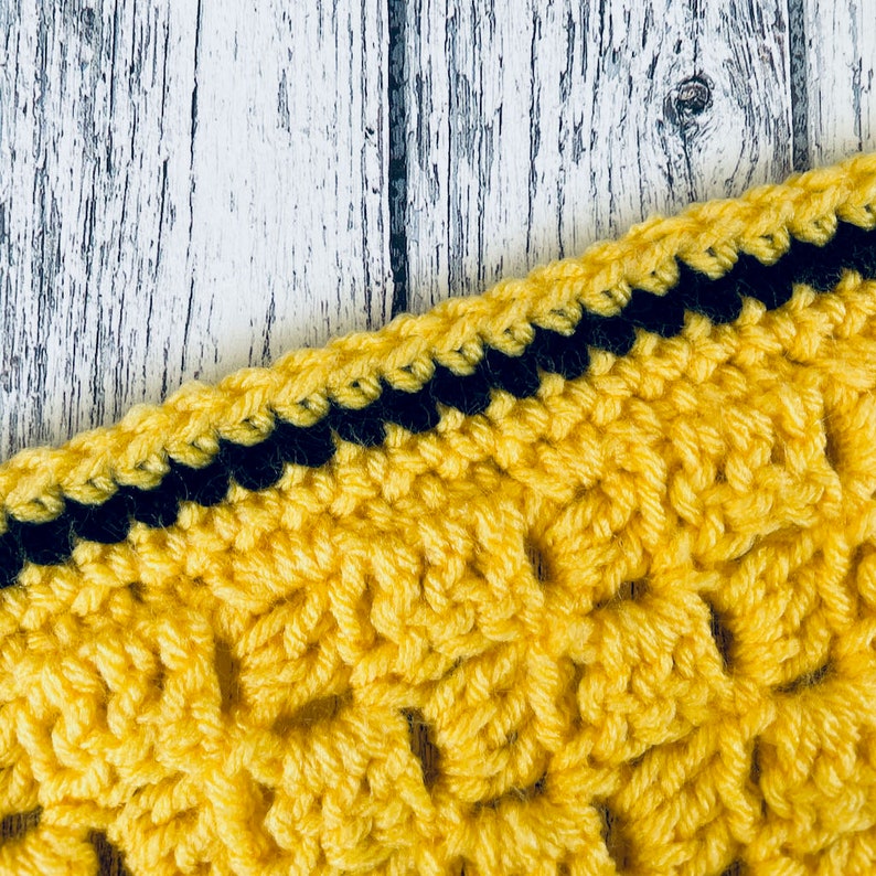 May include: Close-up of a yellow crocheted fabric with a black crocheted border. The fabric has a textured, woven pattern.