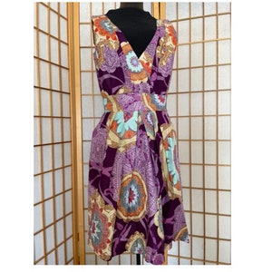 May include: A sleeveless purple dress with a V-neckline and a colorful floral print. The dress has a fitted bodice and a flowing skirt.