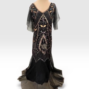 May include: A black floor-length dress featuring a V-neckline and short sheer sleeves. The bodice is heavily embellished with intricate gold, silver, and iridescent beadwork in a symmetrical pattern. The skirt flares into a sheer tulle hem.