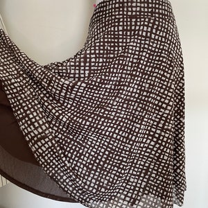 May include: A brown and white patterned skirt. The skirt has a grid-like pattern in brown and white. The skirt is made of a lightweight material and has a flowing design. The skirt is displayed on a mannequin.