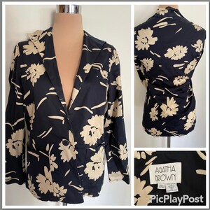 May include: A black and cream floral patterned blazer with a single button closure and a pocket on the left side. The blazer has a label that reads "Agatha Brown" and "100% Cotton" in the bottom right corner.