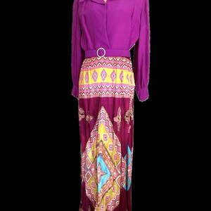 May include: A long purple dress with a geometric print skirt. The skirt is a mix of pink, yellow, blue, and green. The dress has a matching purple belt with a silver buckle.