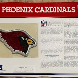 May include: A vintage patch featuring the Phoenix Cardinals logo. The patch is red, white, and silver with a red cardinal bird with a black beak and yellow accents. The patch is surrounded by a white border and has a silver outline. The text "Phoenix Cardinals" is printed in black at the top of the patch.