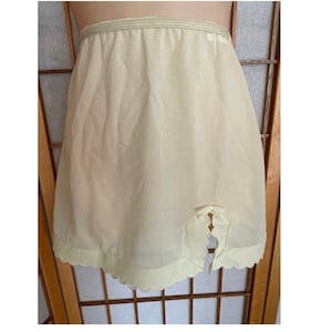 May include: A pale yellow nylon slip with a scalloped hem and a bow at the back.