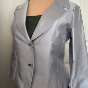 May include: A silver satin blazer with a single button closure and long sleeves. The blazer has a classic, tailored fit and a subtle sheen.