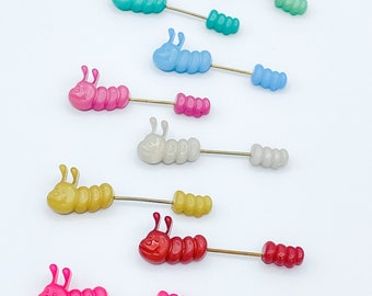 May include: Assortment of colorful plastic caterpillar pins with a gold wire. The caterpillars are in various colors including pink, red, yellow, white, blue, and green.