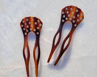 Puede incluir: Dos peines para el cabello de carey marrón con detalles de diamantes de imitación transparentes. Los peines tienen una parte superior decorativa festoneada y una base de tres púas.