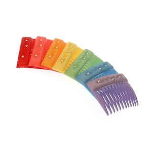 Puede incluir: Un juego de peines para el cabello de colores arcoíris con un diseño decorativo. Los peines están dispuestos en forma de arcoíris, con el peine rojo en la parte superior y el peine morado en la parte inferior.