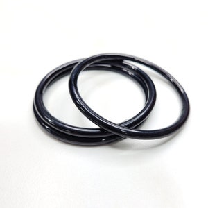 May include: Three black bangle bracelets stacked together on a white background.