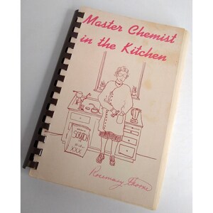 May include: A vintage cookbook titled "Master Chemist in the Kitchen" with a hand-drawn illustration of a woman in a kitchen. The cookbook is bound with a brown spiral binding.
