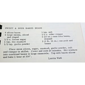 Op de afbeelding: Een gedrukte receptkaart met de titel Sweet & Sour Baked Beans. De tekst bevat ingredi&euml;nten zoals 8 plakjes spek, 4 grote uien, 1/2 kop bruine suiker, 1 tl droge mosterd, 1/2 tl knoflookpoeder, 1 tl zout, 1/2 kop appelazijn, twee blikken van 15 oz limabonen en twee blikken van 1 lb 11 oz varkensvlees met bonen, gevolgd door kookinstructies en de naam Lorrie Watt.