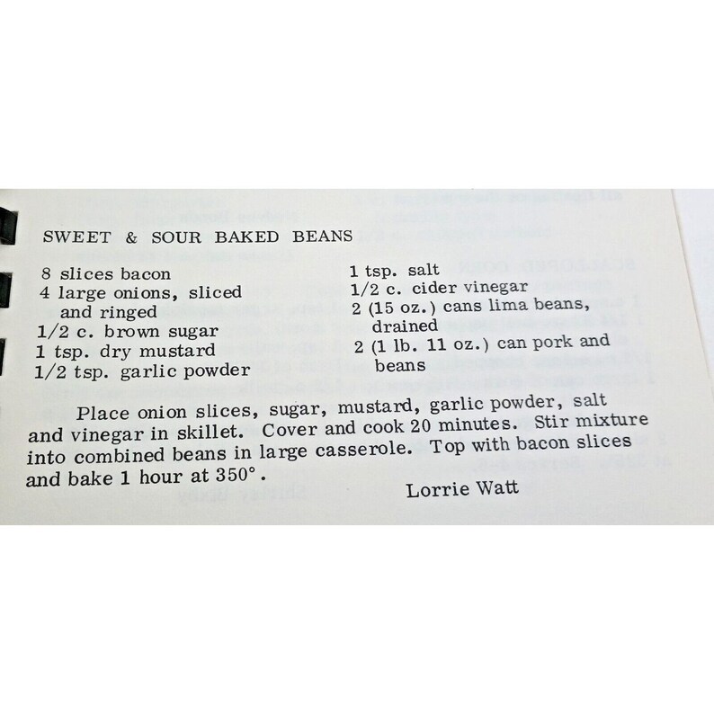 Op de afbeelding: Een gedrukte receptkaart met de titel Sweet & Sour Baked Beans. De tekst bevat ingredi&euml;nten zoals 8 plakjes spek, 4 grote uien, 1/2 kop bruine suiker, 1 tl droge mosterd, 1/2 tl knoflookpoeder, 1 tl zout, 1/2 kop appelazijn, twee blikken van 15 oz limabonen en twee blikken van 1 lb 11 oz varkensvlees met bonen, gevolgd door kookinstructies en de naam Lorrie Watt.