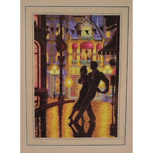 May include: A cross-stitch embroidery depicting a silhouette of two figures dancing in a rain-slicked city street at night. The background features illuminated building windows, street lamps, and festive bunting in shades of yellow, purple, and black.