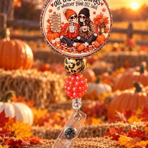 Peut inclure: Un enrouleur de badge circulaire illustré de deux squelettes assis avec des tasses, entourés de citrouilles et de feuilles d'automne. Le texte indique all the fall things or whatever Blink-182 said. Il comprend une perle léopard et une perle rouge texturée.