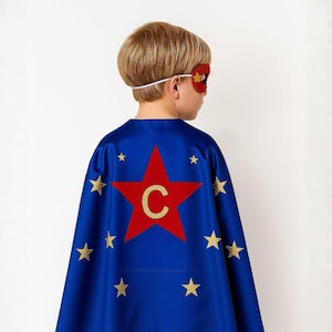 May include: A blue superhero cape with a red star and a gold letter "C" in the center. Gold stars are scattered across the cape. A red eye mask with a gold star is also visible.