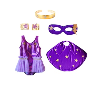 May include: A purple metallic leotard with gold star accents and light purple tulle ruffles, a matching purple cape with gold stars, a purple eye mask with gold stars and a lightning bolt, two gold wrist cuffs with pink stars, and a gold headband.