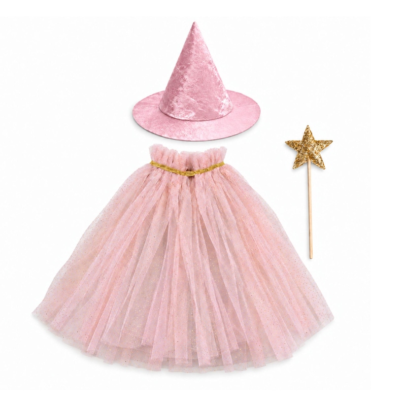 May include: A pink velvet pointed hat, a pink tulle cape with a gold glittery waistband, and a gold glittery star wand on a thin wooden stick. The set features soft pink fabric textures and shimmering gold accents throughout the three separate pieces.