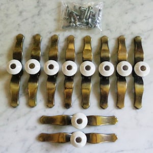 Puede incluir: Diez tiradores de cajón dorados con pomos de porcelana blanca. Los tiradores miden aproximadamente 7,5 cm de largo y tienen una forma curva. Los pomos tienen un diámetro de aproximadamente 2,5 cm. También se incluyen tornillos.