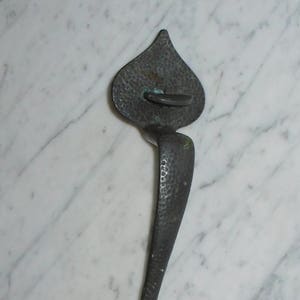 May include: A hammered metal door handle with a heart-shaped bottom and a pointed top. The handle is dark grey and has a textured surface.