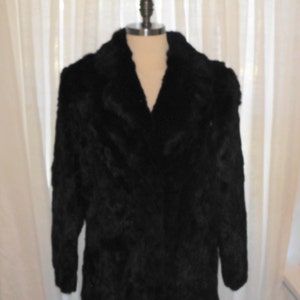May include: A long black fur coat with a collar. The coat is on a white mannequin.