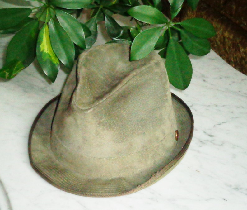 May include: A green felt fedora hat with a brown leather band and a metal button on the side.