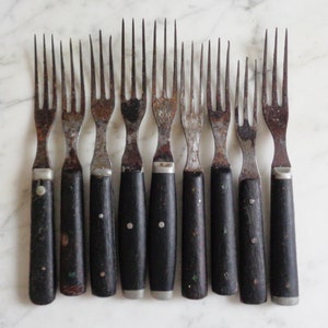 Puede incluir: Conjunto de diez tenedores vintage con mangos de madera negra. Los tenedores son de metal y tienen un aspecto rústico y desgastado.