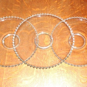 Könnte beinhalten: Drei klare Glas-Kuchenplatten mit perlenbesetzten Rändern. Die Platten sind übereinander gestapelt.