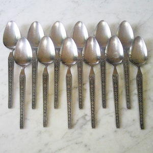 May include: A set of 12 silver spoons with an ornate design. The spoons have a heart-shaped design at the top of the handle.