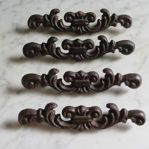 Puede incluir: Cuatro tiradores de cajón de hierro fundido ornamentados con un acabado marrón oscuro. Cada tirador presenta un diseño de desplazamiento con un adorno central.