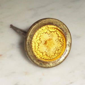 May include: A gold-toned bottle stopper with a decorative, yellow glass top featuring a floral design.