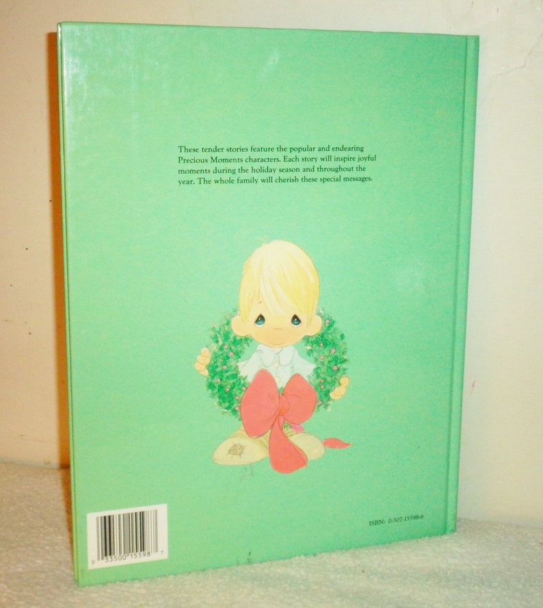 May include: The back cover of a book featuring a Precious Moments character holding a Christmas wreath. The text on the back cover reads: "These tender stories feature the popular and endearing Precious Moments characters. Each story will inspire joyful moments during the holiday season and throughout the year. The whole family will cherish these special messages."