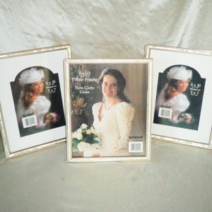 May include: Three silver picture frames with a beaded border. The center frame has a photo of a bride in a white dress and the text "8x10 Photo Frame Non-Glare Glass". The other two frames have a photo of a bride in a white dress with a white hat and the text "8x10 Matted to 5x7".