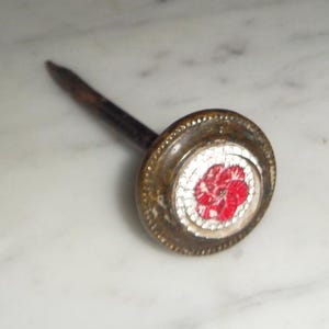 May include: A decorative nail with a round brass head featuring a red and white flower design.