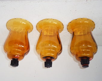 May include: Three amber glass candle holders with a scalloped rim and a black metal base.